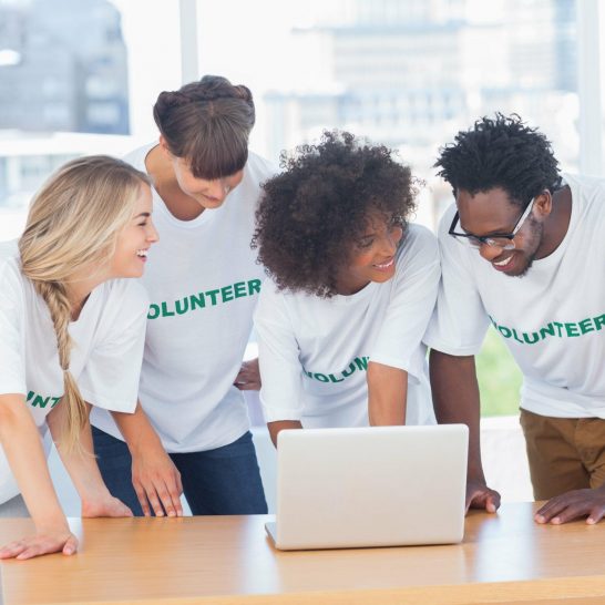 smiling-volunteers-working-together-laptop-min-scaled.jpg